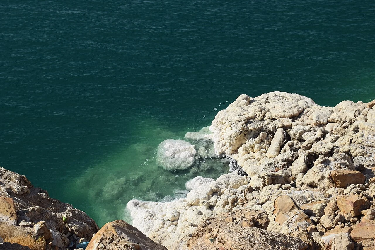 White salt deposits on rocks beside blue water on the Jordanian Dead Sea coast